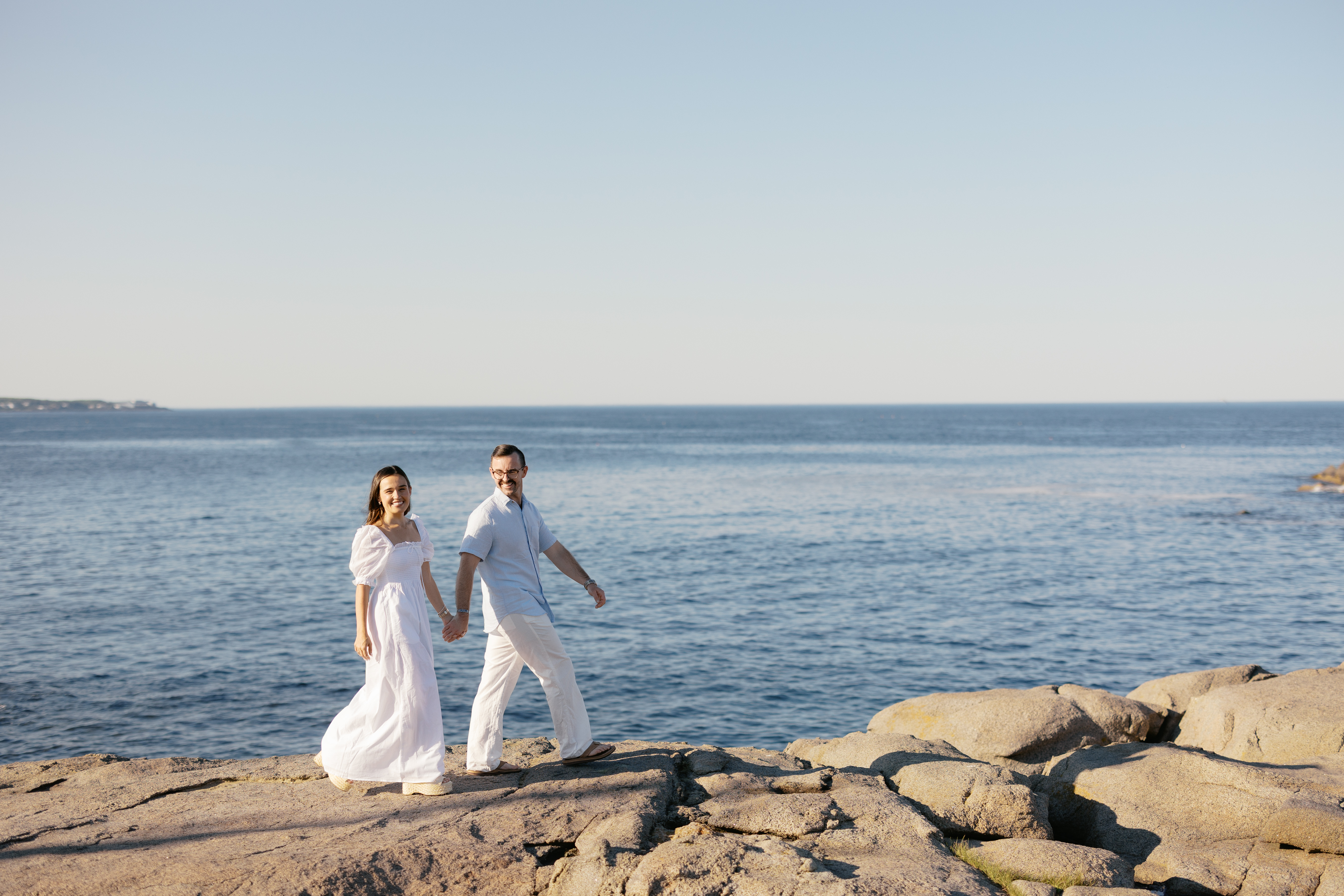 Julianne and Morgan walking hand in hand along the rocky Maine coastline